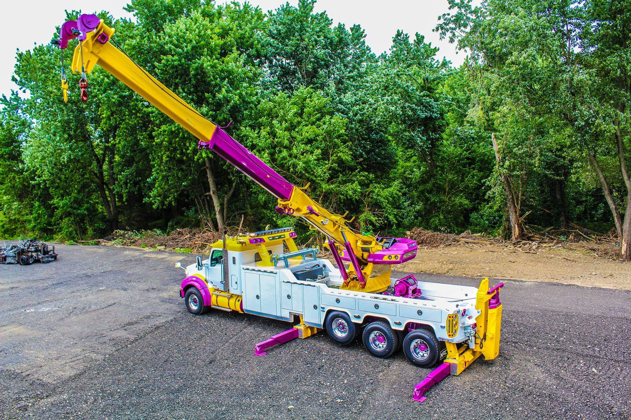 Brightly colored wrecker truck in operation, showcasing rigging and recovery equipment among trees.