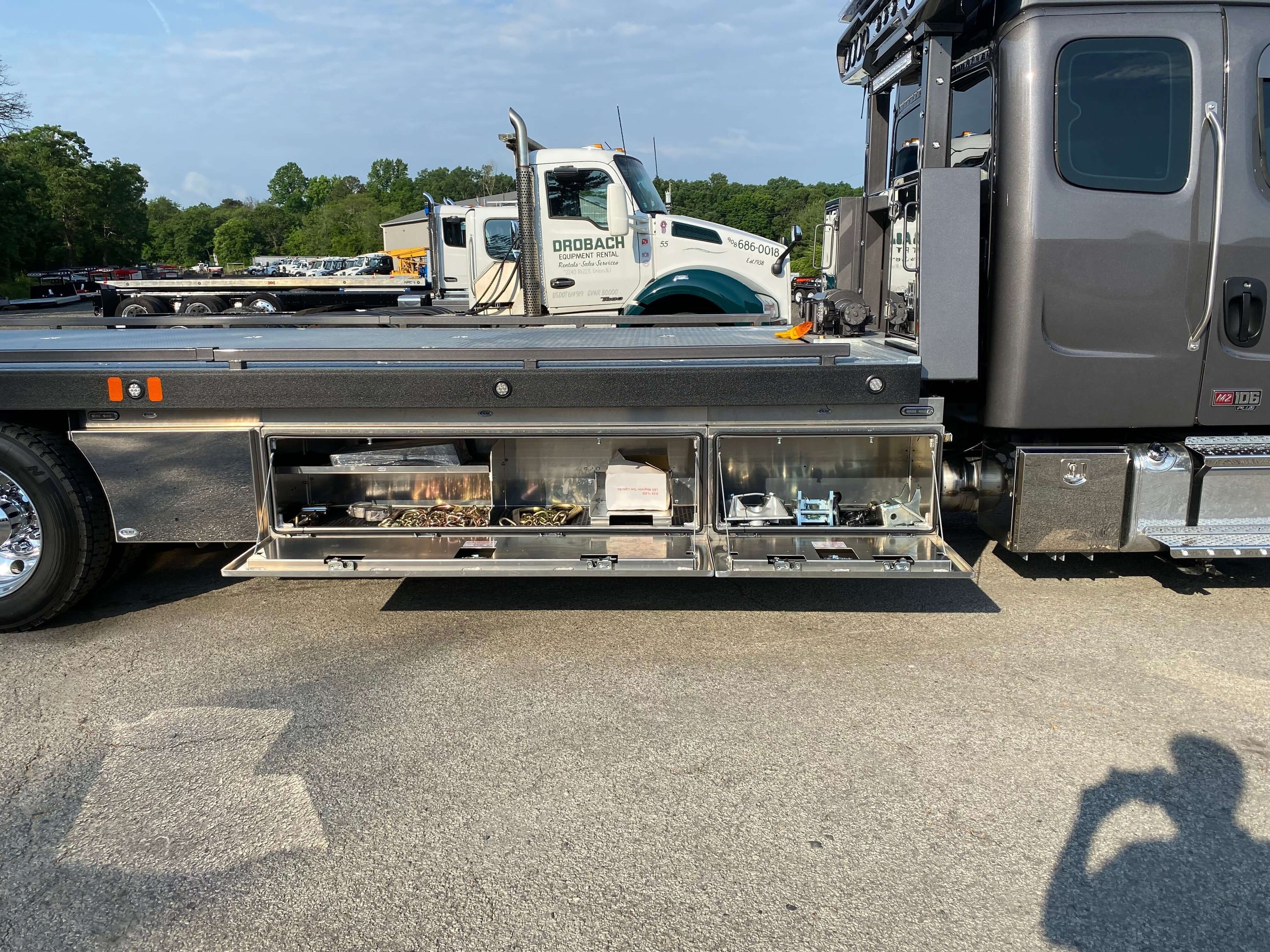 truck toolboxes with open compartments displaying organized toolbox parts & accessories on the side of a car carrier tow truck.