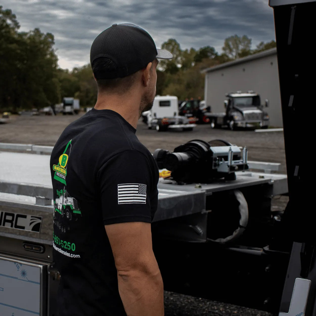 standing next to a car carrier tow truck wearing battelini's trucking t-shirt