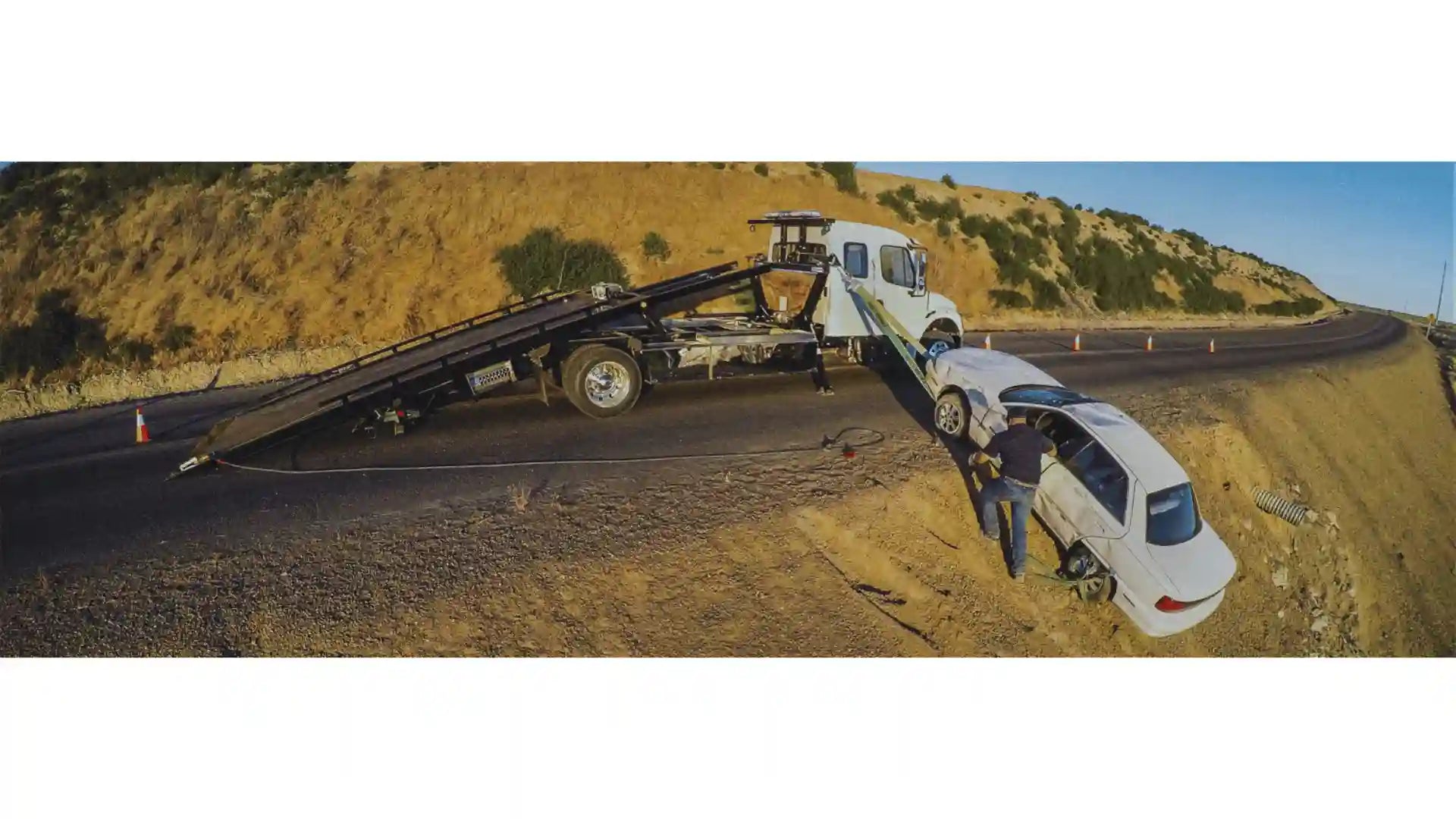 Tow truck towing a damaged car on a rural road using the in the ditch sidepuller
