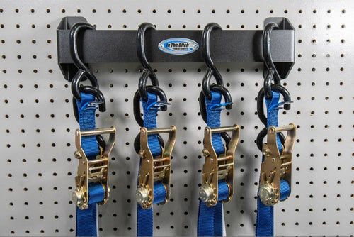 In The Ditch Tie Down Strap Hanger mounted on a pegboard, holding four blue ratchet straps with gold hardware. Durable aluminum with black powder coat finish.