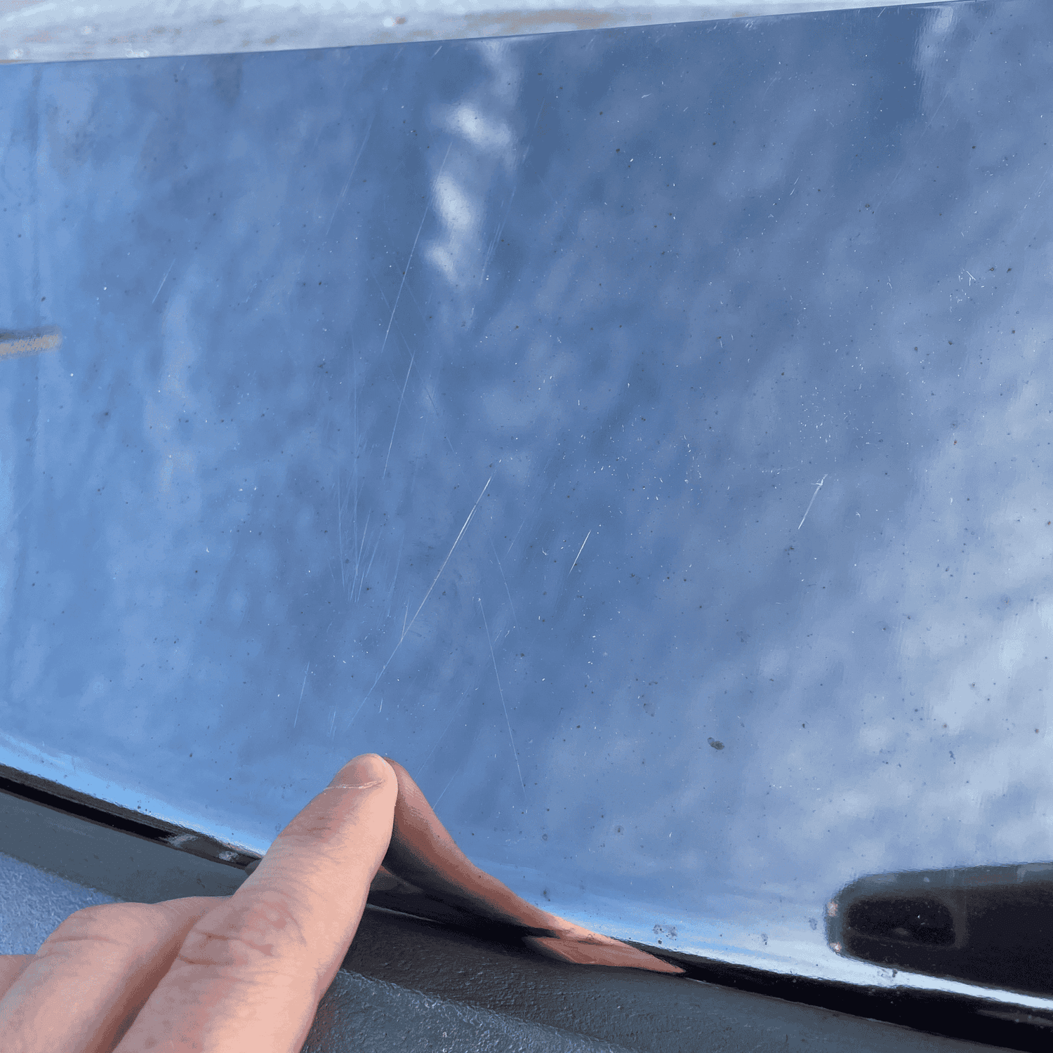 Detailed view of scratches on a used stainless steel Paccar sun visor for Kenworth W900. Finger pointing at blemishes on the reflective surface.