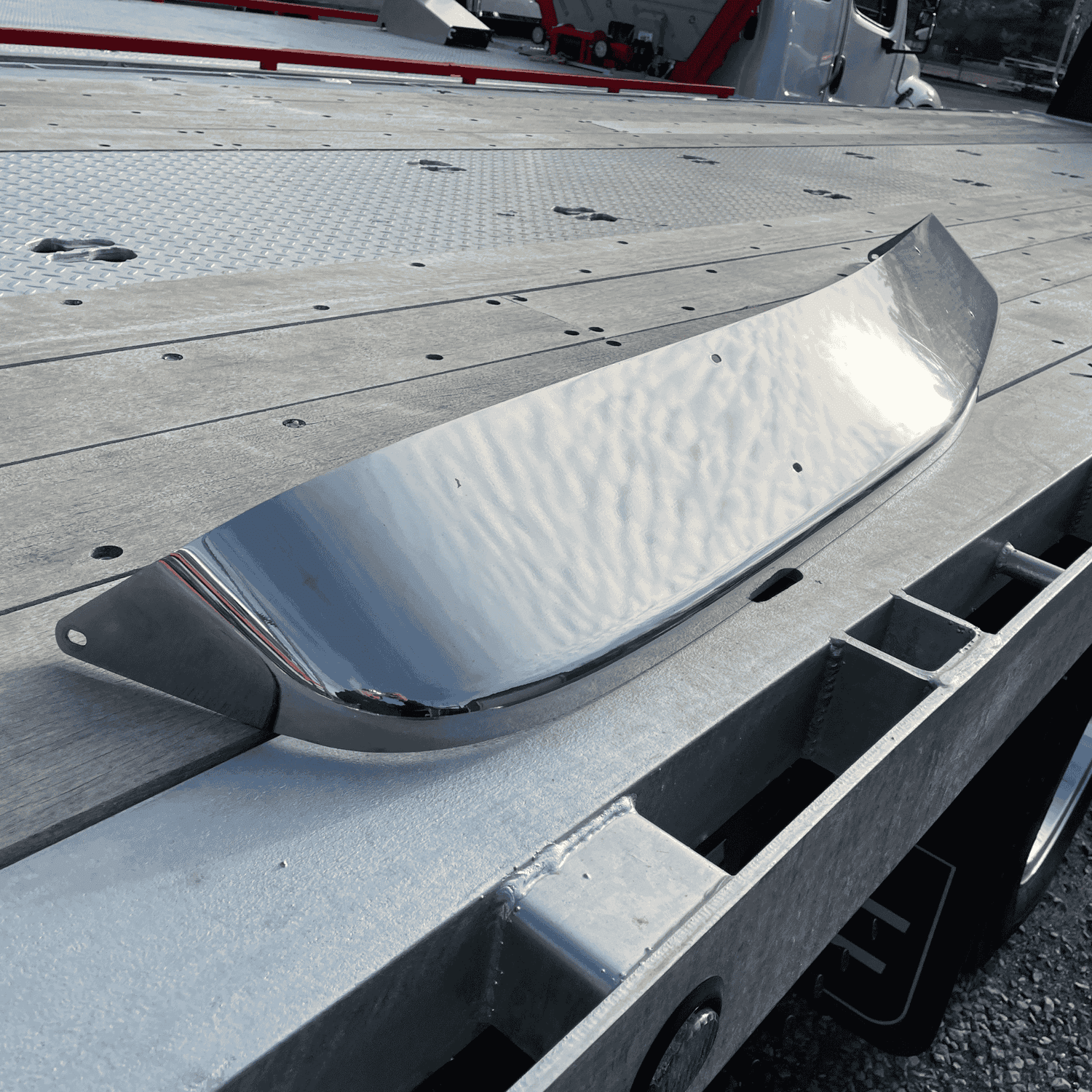 Side view of a used stainless steel Paccar sun visor for Kenworth W900, placed on a truck bed. Slight imperfections visible on the polished surface.